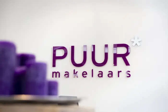 The logo of “PUUR makelaars” in bold purple letters with an asterisk symbol, set against a blurred background with matching purple tones, representing the company’s corporate identity.