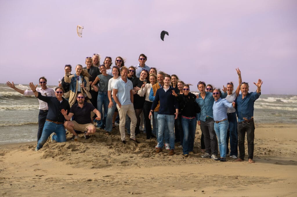 Group enjoying beach with kite surfers in background.