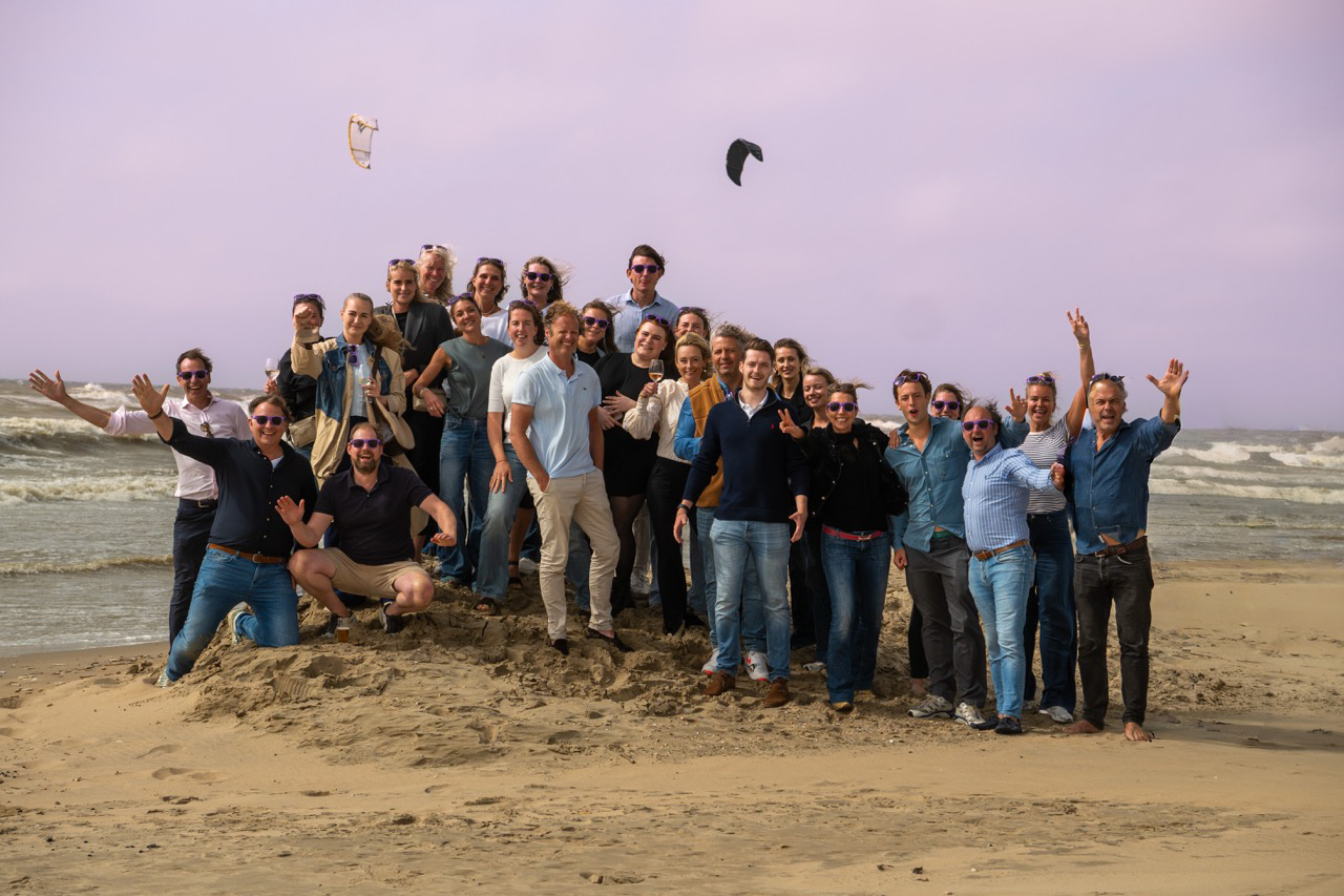 Group enjoying beach with kite surfers in background.