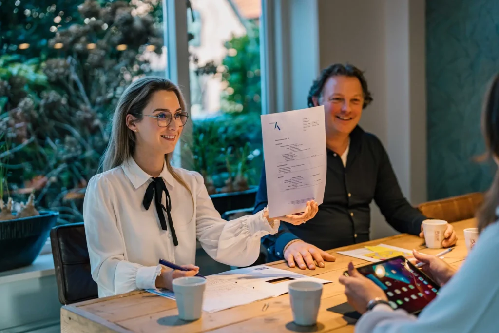 Two professionals engage in a document review. The setting includes a table with coffee cups and electronic devices, highlighting a focused business discussion.