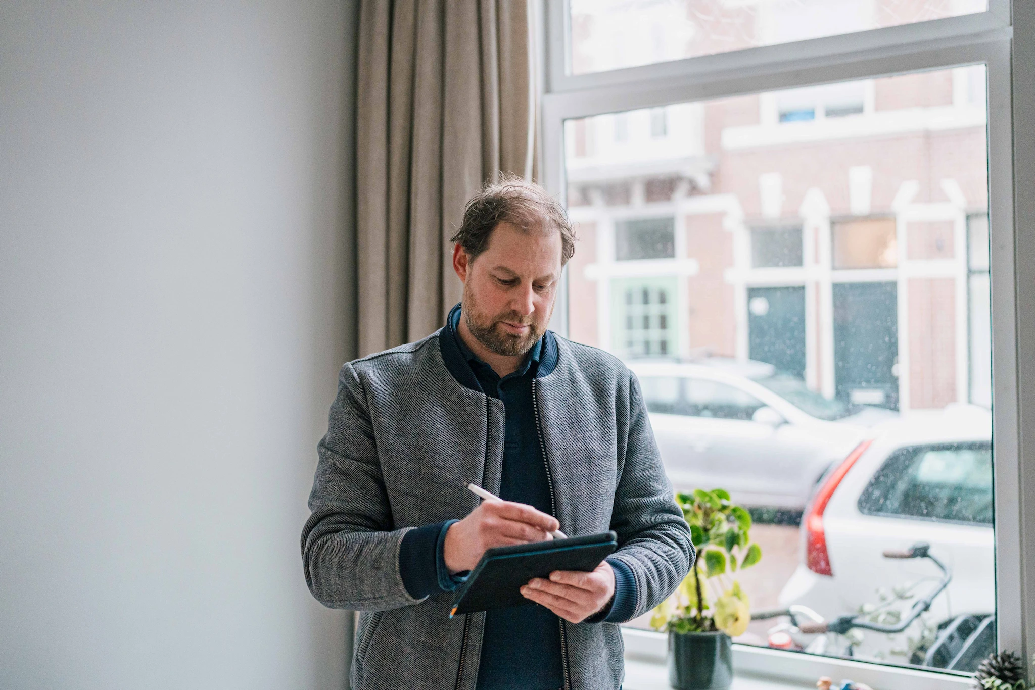 Een man die bij een raam staat en met een stylus op een tablet schrijft.