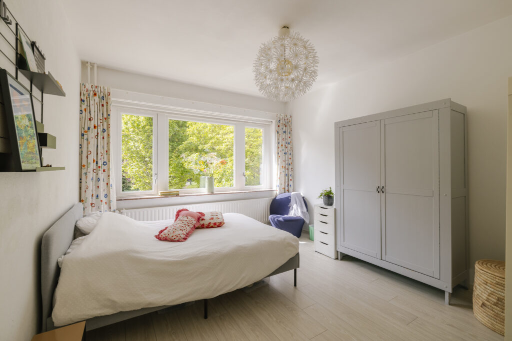 Bright bedroom with large window and white furniture.