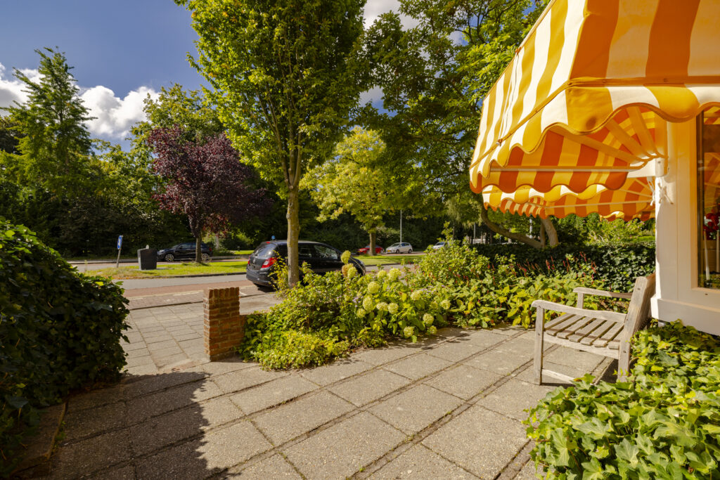 Sunny patio with yellow-striped awning and trees.