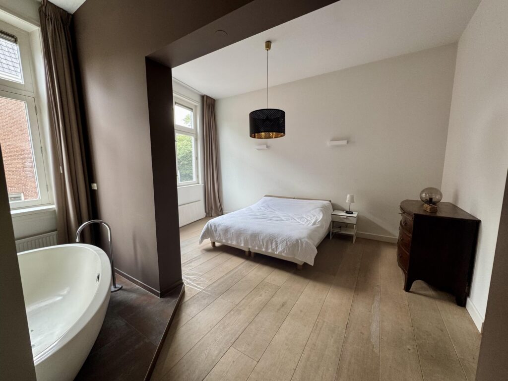 Modern bedroom with bathtub and wooden floors.