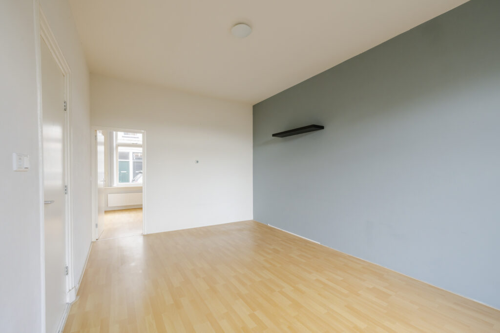 Empty room with wooden flooring and light walls.