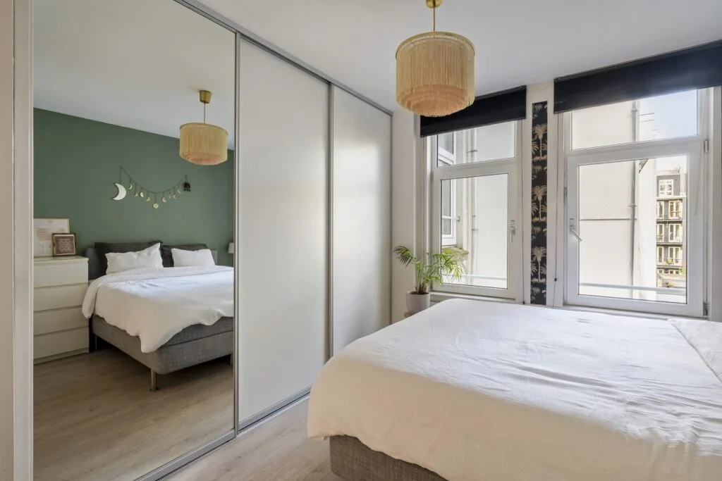 Modern bedroom with mirrored closet and green wall.