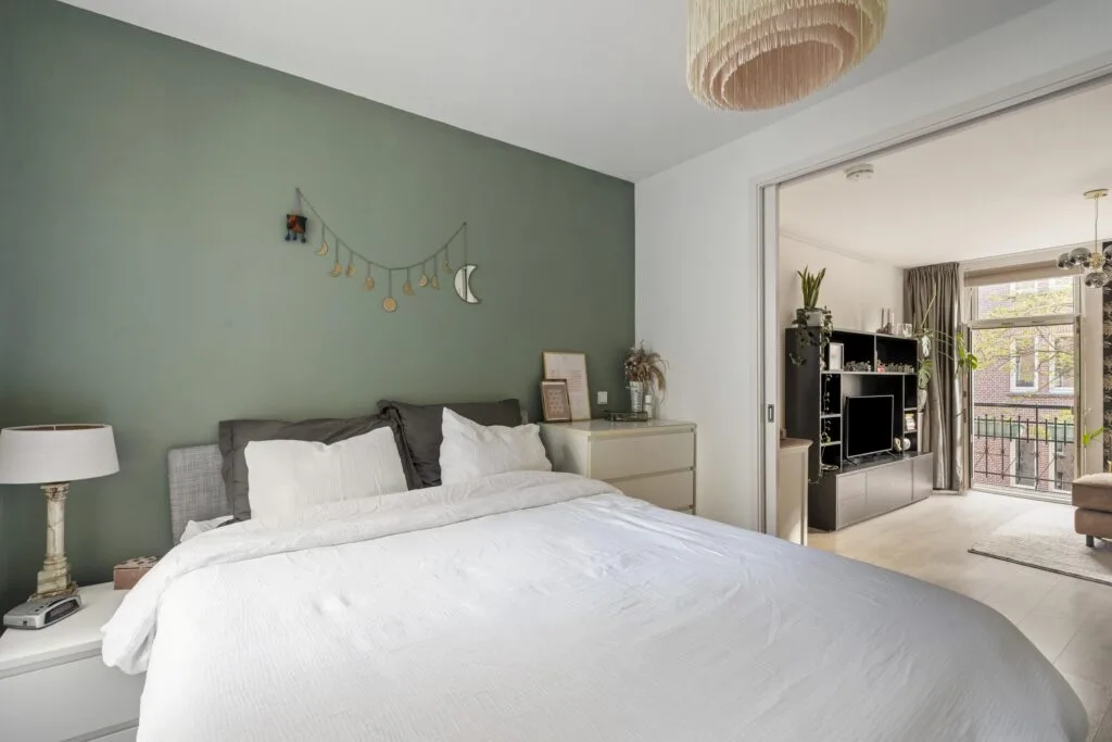Cozy bedroom with green accent wall and lamp.