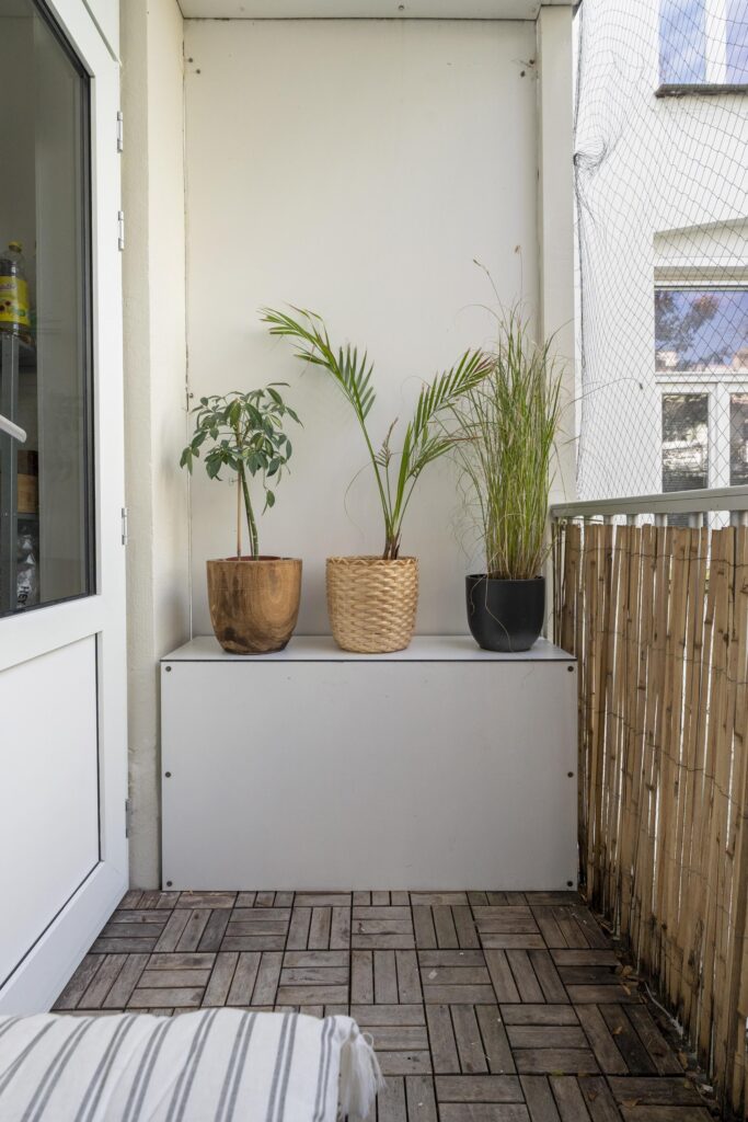 Small balcony with potted plants and wooden floor.