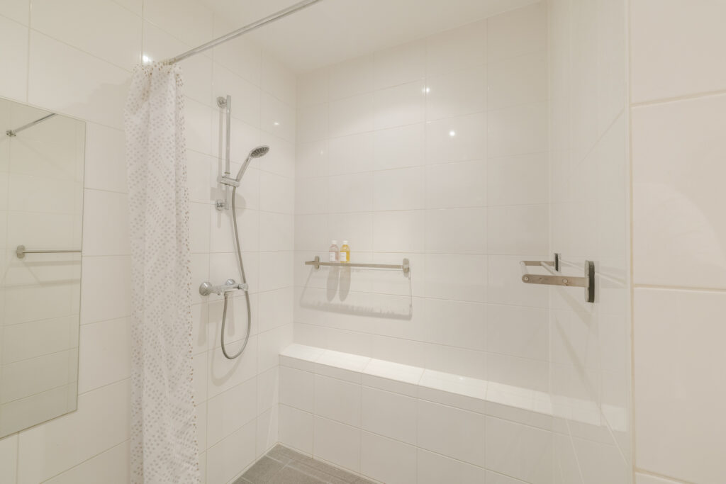 Modern white tiled shower with curtain and bottles.