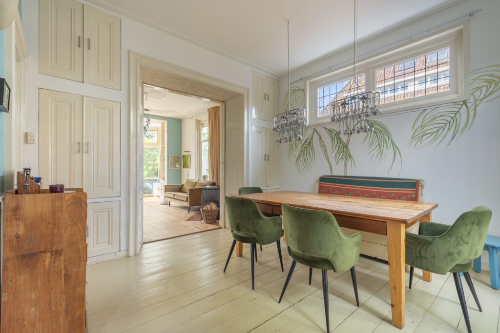 Spacious dining room with green chairs and chandelier.