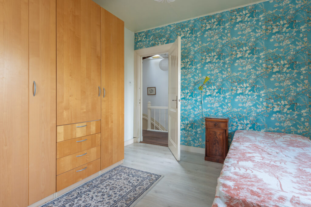 Cozy bedroom with floral wall and wooden furniture.
