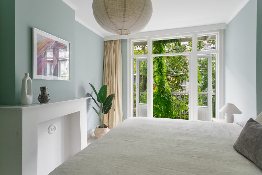 Bright bedroom with large windows and green view.