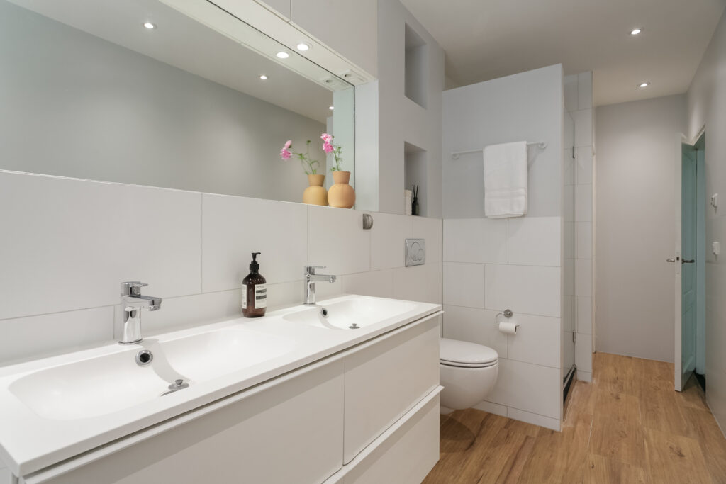 Modern bathroom with double sinks and wood flooring.