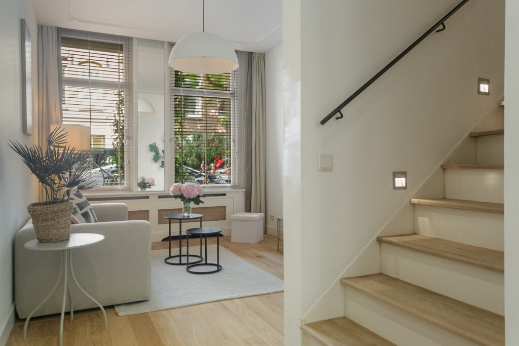 Modern living room with stairs and large windows.
