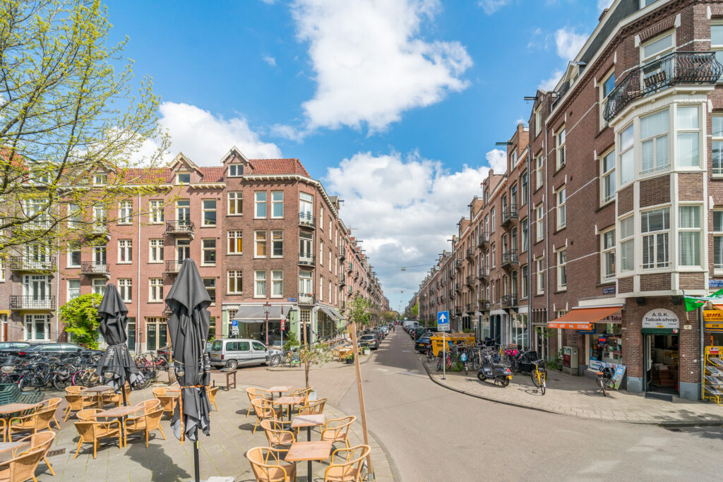 Sunny urban street with outdoor seating and shops.