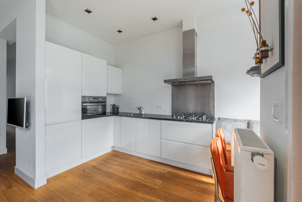 Modern kitchen with white cabinets and wood flooring.