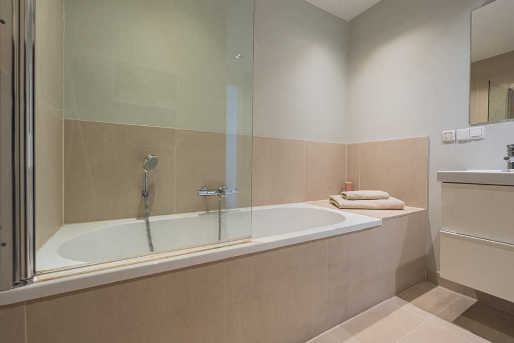 Modern bathroom with bathtub and towels on edge.