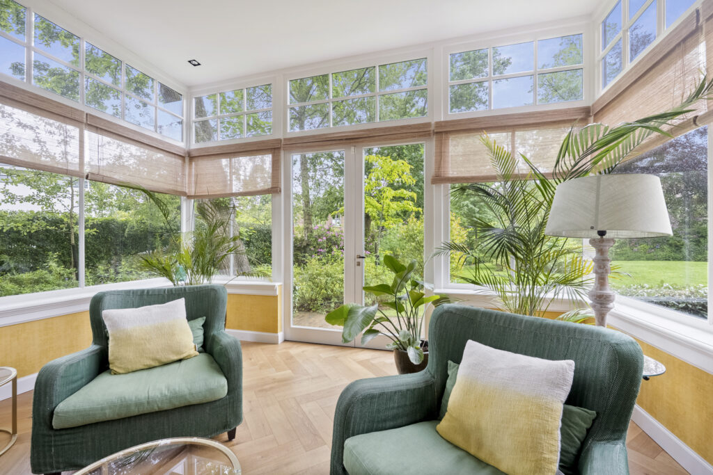 Bright sunroom with green chairs and plants.