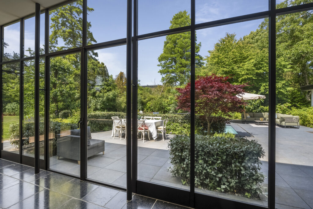 Patio with chairs and garden view through glass doors.