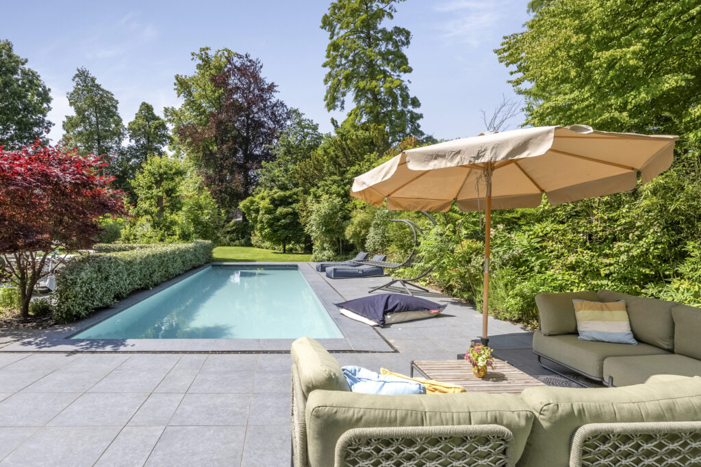 Sunny backyard pool with patio and furniture.