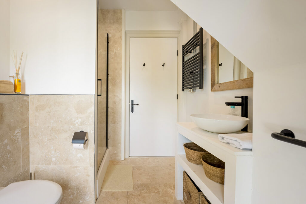 Modern bathroom with beige tiles, white sink, wicker baskets.