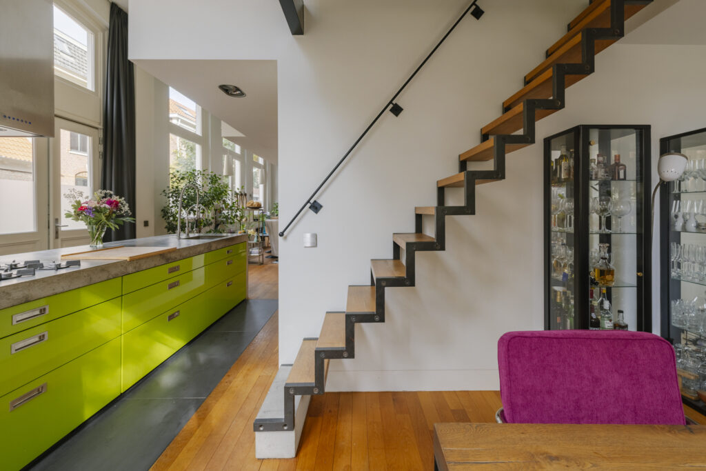 Modern kitchen with green cabinets and zigzag stairs.