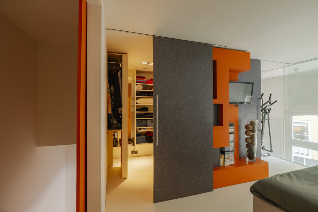 Modern bedroom with sliding closet and orange shelving.