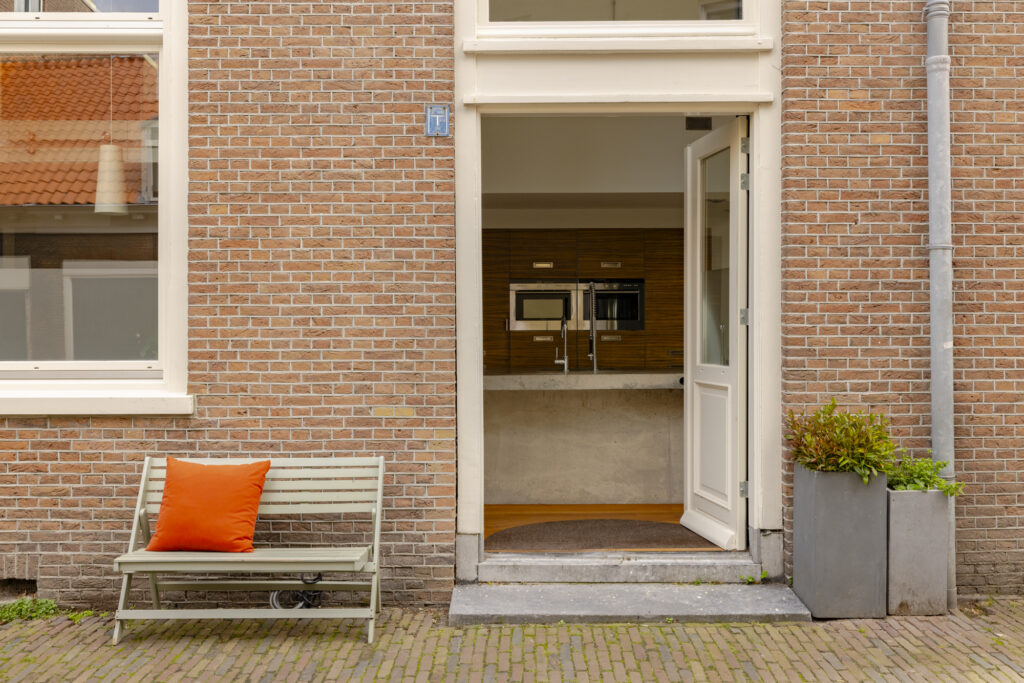 Open door, brick wall, bench with orange pillow