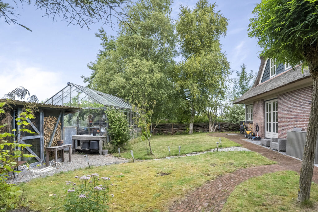 Backyard garden with greenhouse and brick house.