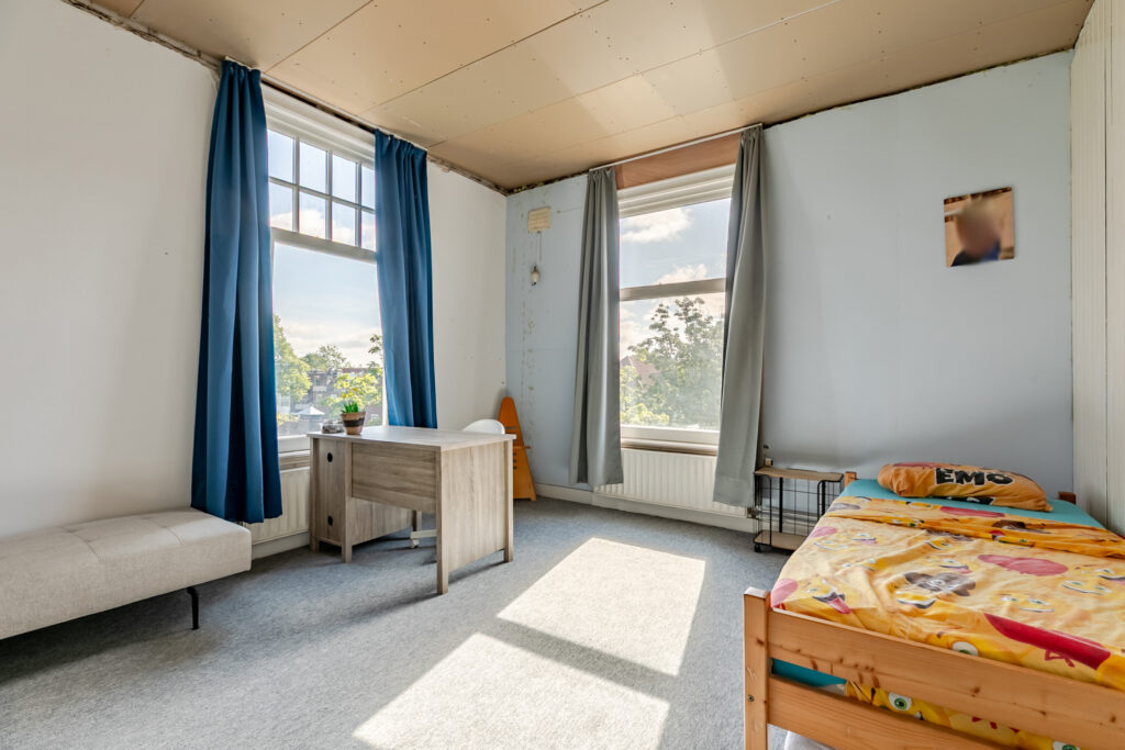 Bright room with desk, bed, and large windows.