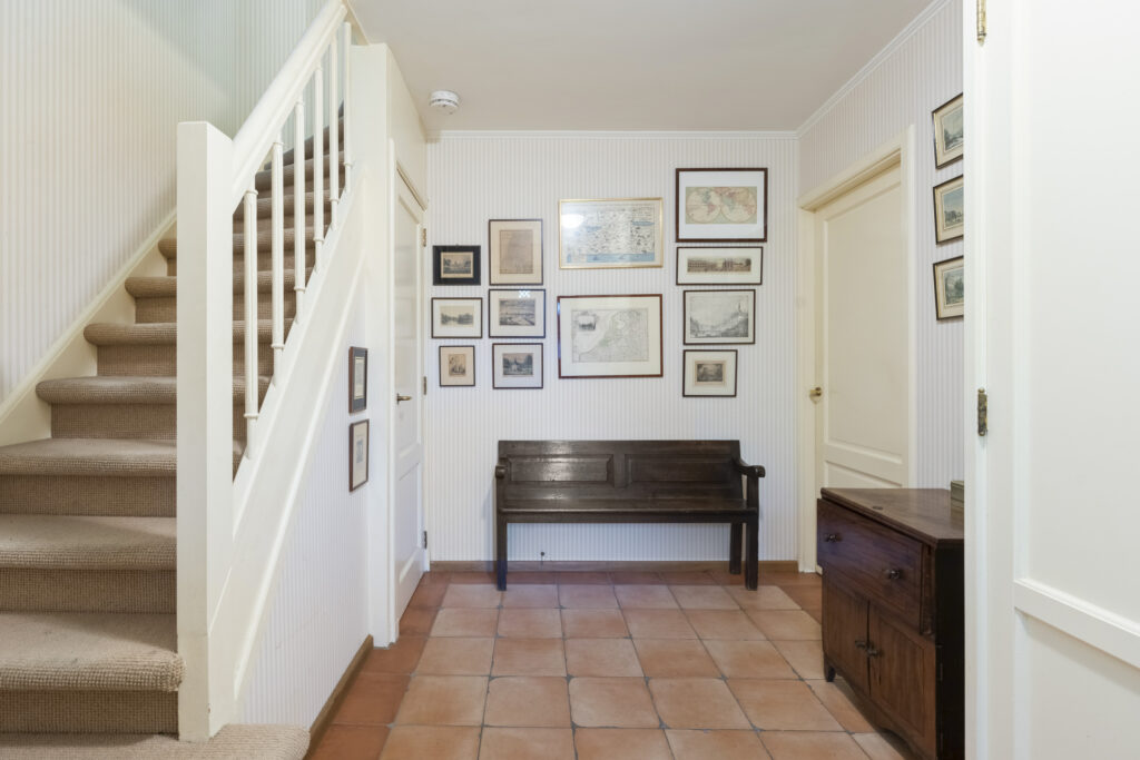 Hallway with stairs, bench, and framed pictures.