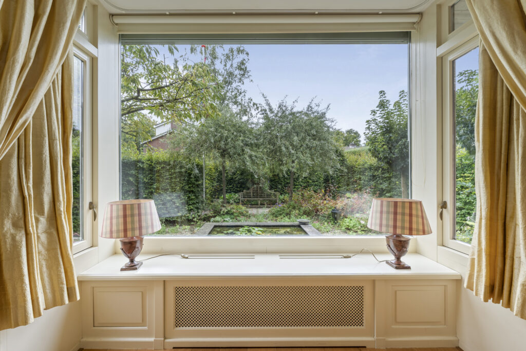 Window view of garden with pond and trees.