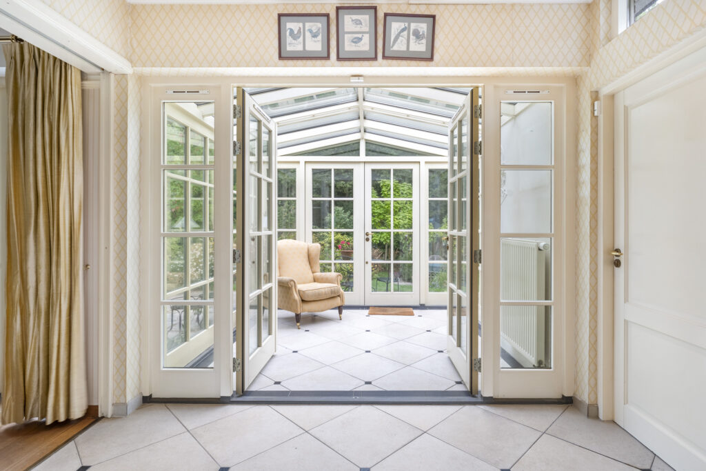 Sunny conservatory with glass doors and armchair.
