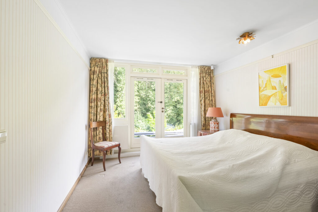 Bright bedroom with large window and wooden furniture.