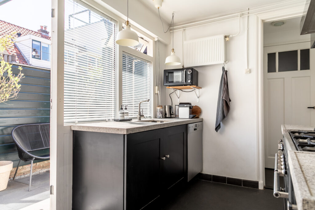 Modern kitchen with black cabinets and window blinds.
