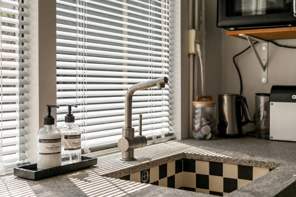 Modern kitchen sink with blinds and soap bottles.