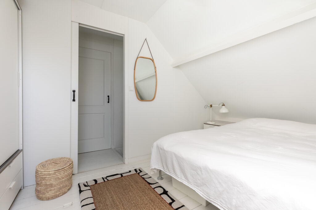 Minimalist white bedroom with bed, mirror, and lamp.