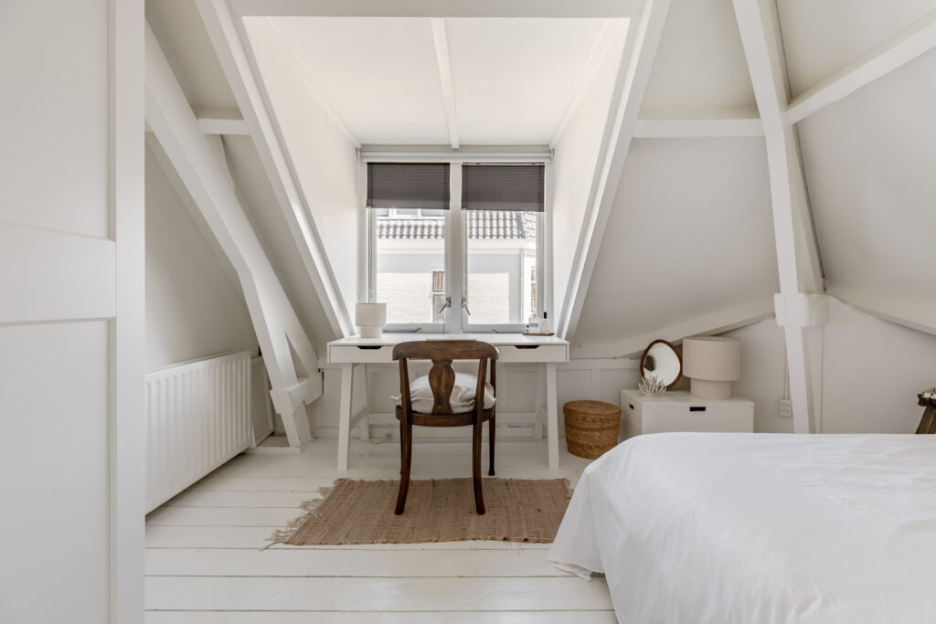 Minimalist attic bedroom with white decor and desk.