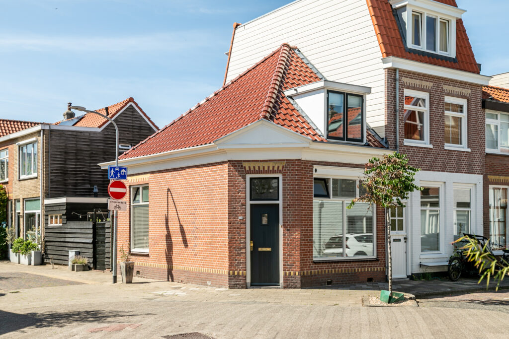 Corner brick house with red roof on a sunny street.