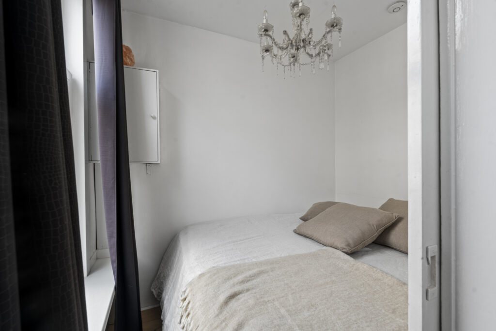 Small bedroom with chandelier and two pillows.