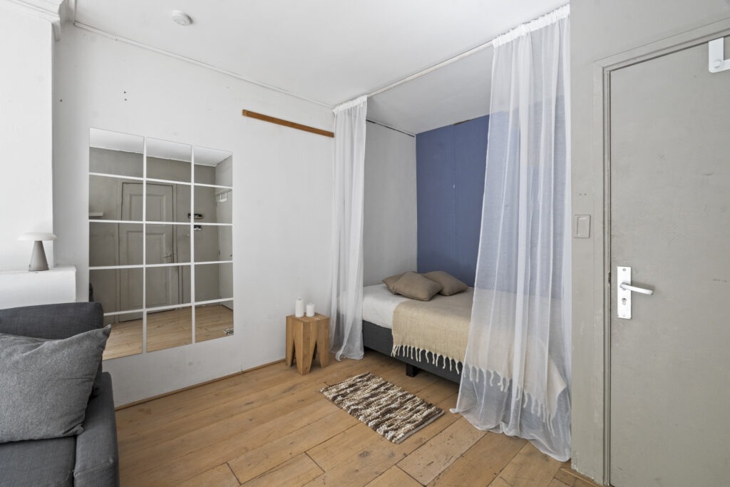 Cozy minimalist bedroom with sheer curtains and mirror.