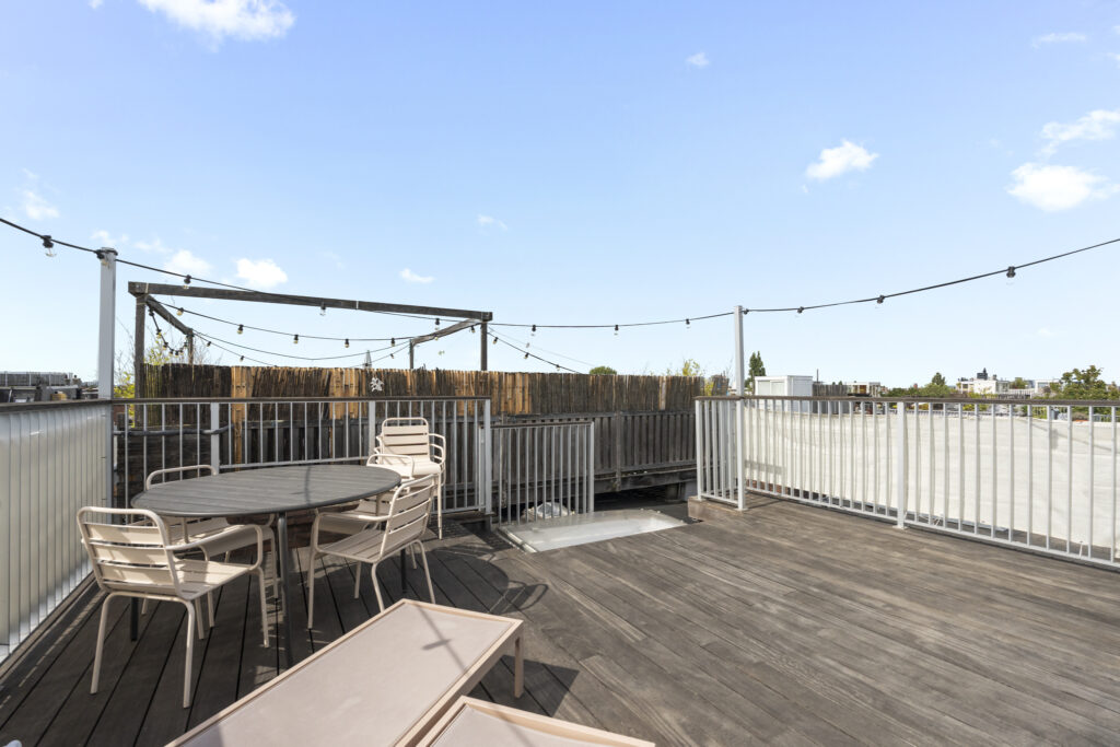 Outdoor rooftop wooden deck with chairs and string lights.