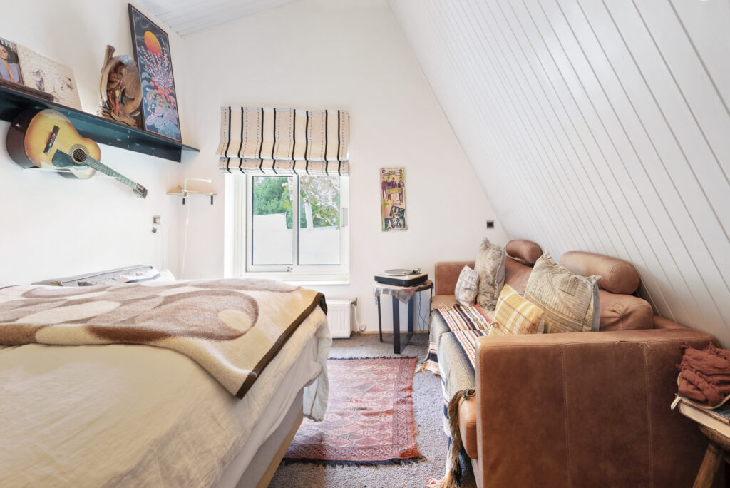 Cozy attic bedroom with guitar and artwork decor.