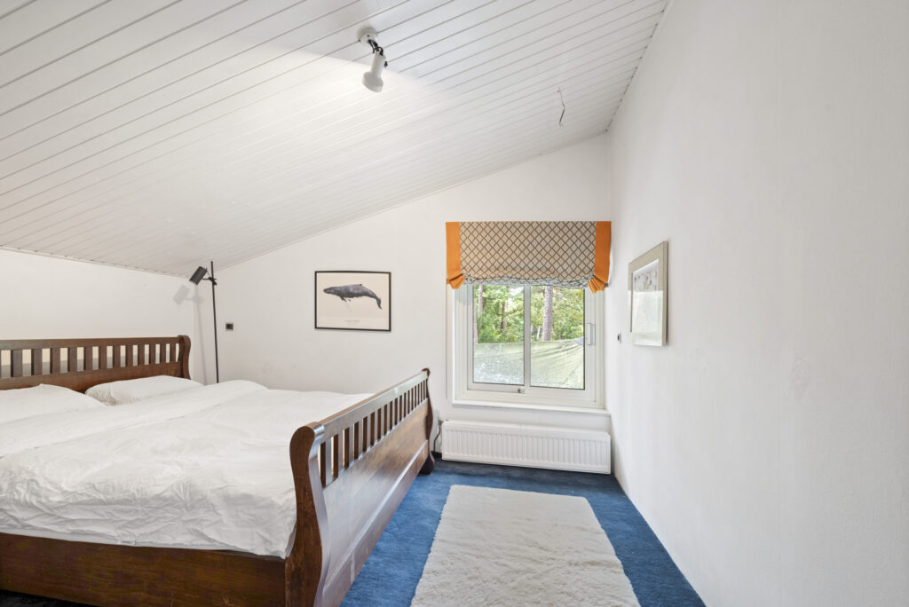 Cozy bedroom with wooden bed and window view.