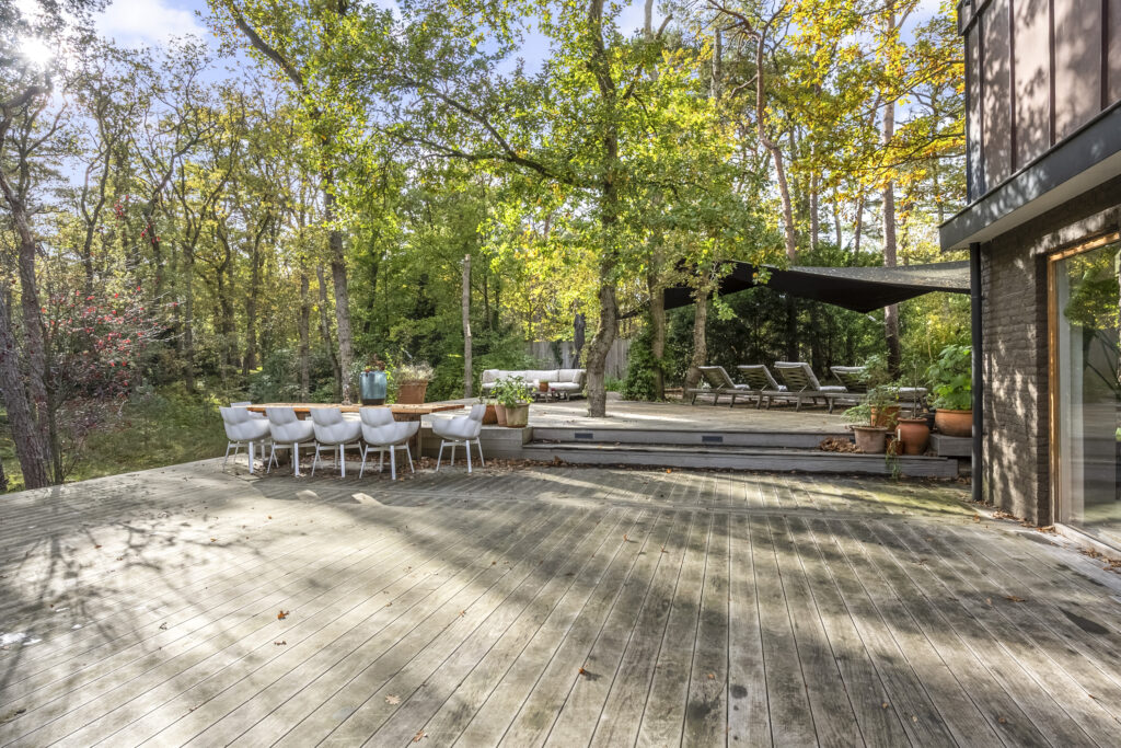 Spacious wooden deck with outdoor furniture amidst trees.