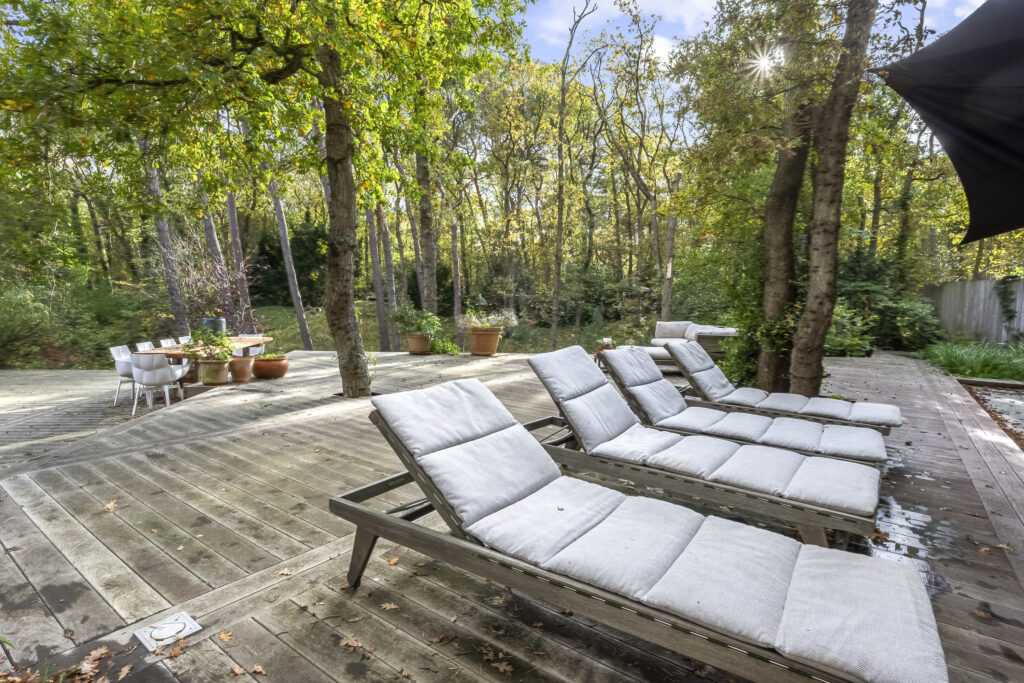 Wooden deck with lounge chairs in forest setting.