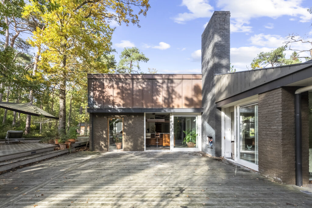 Modern house with large deck amidst trees.