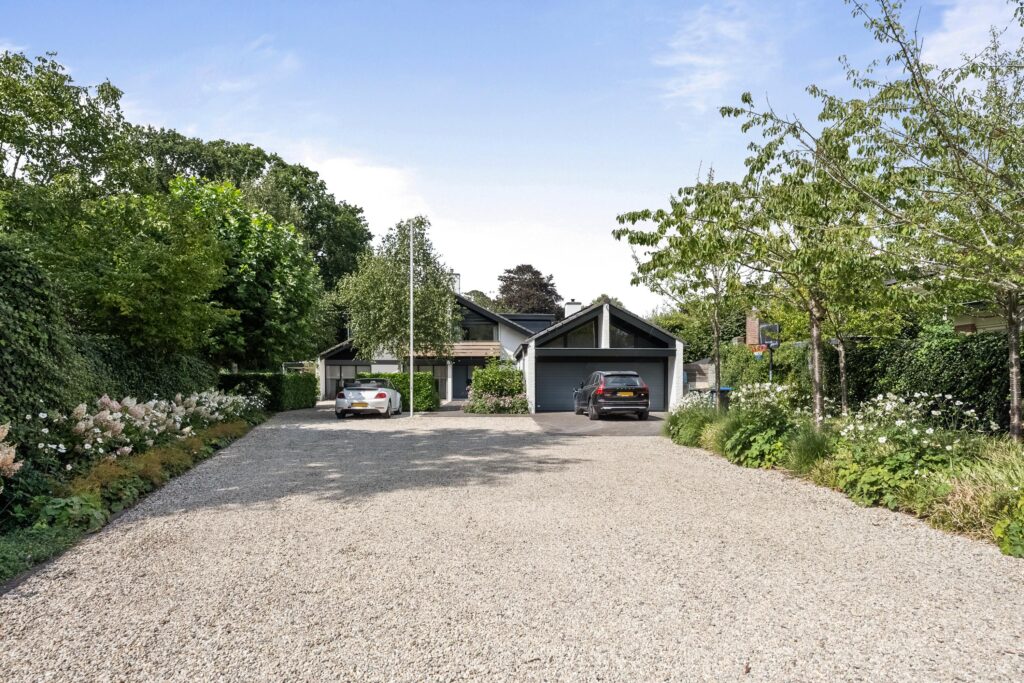 Gravel driveway leading to modern house with two cars.
