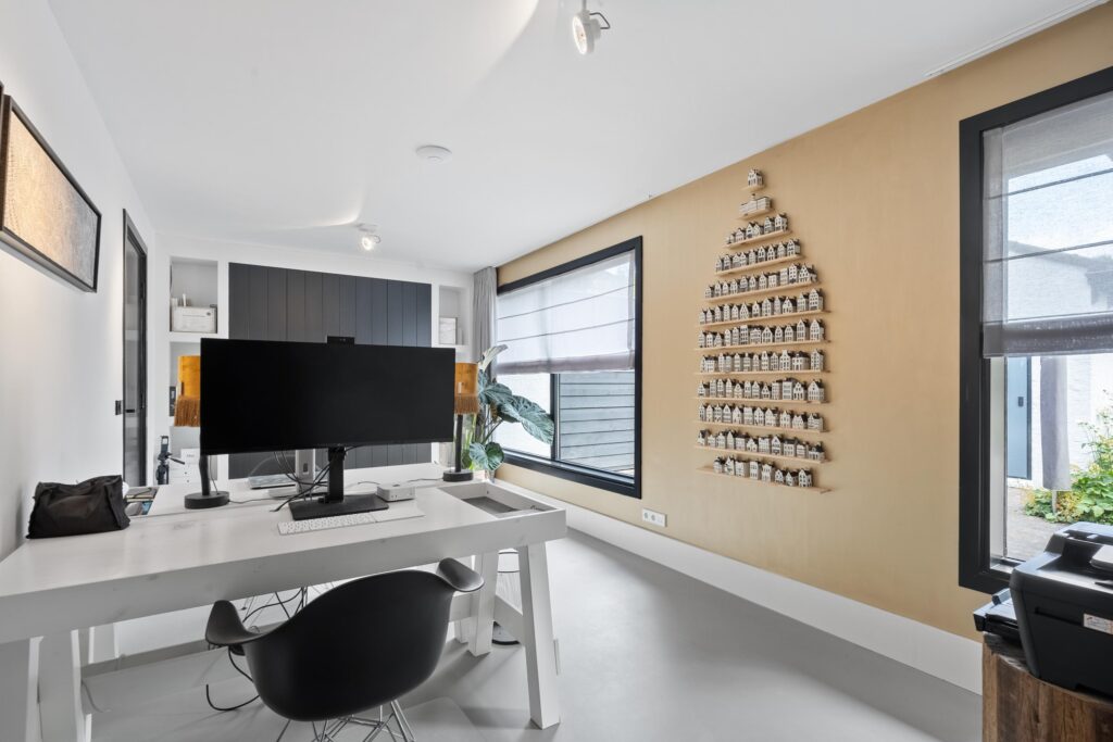 Minimalist home office with wall decor and large windows.