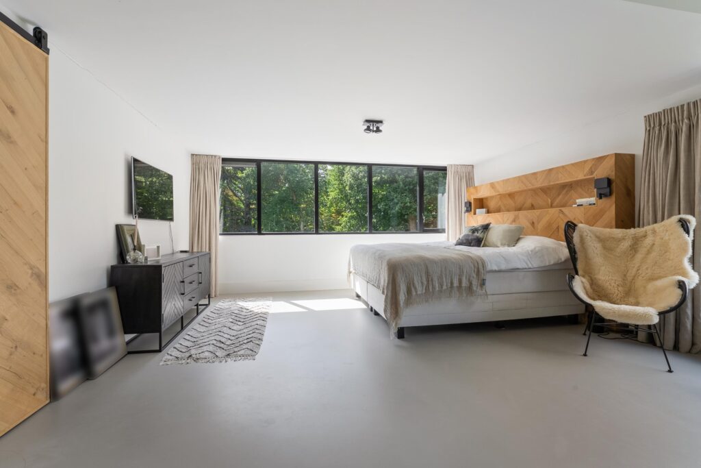 Modern bedroom with large windows and wooden accents.
